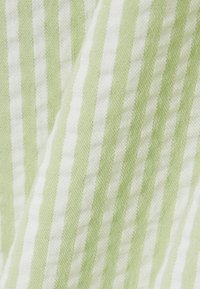 Witte stof met verticale lichtgroene strepen en een subtiele, gestructureerde weving, weergegeven met zachte plooien en schaduwen.