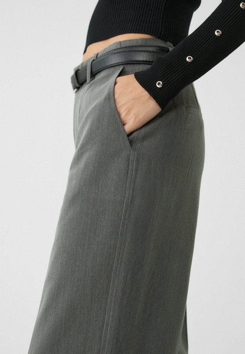 Pantalons gris sur mesure avec un motif de rayures verticales subtil, dotés de poches latérales et d'une ceinture en cuir noir. Le tissu a une texture lisse.