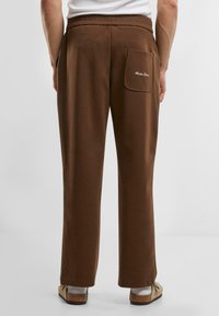 Brown elastic waistband pants feature a straight-leg design with a back pocket. Soft fabric with a smooth texture. Casual overall look.