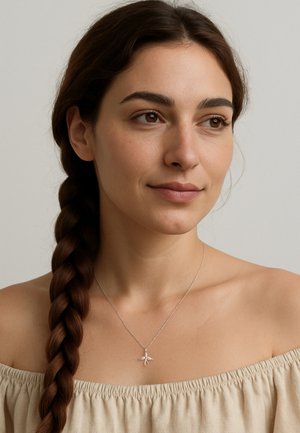 Silberne Halskette mit einem filigranen Schmetterlingsanhänger, getragen von einem Modell mit geflochtenem Haar, vor einem neutralen Hintergrund.