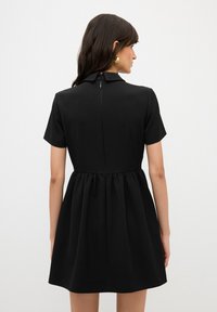 Vestido negro de manga corta con un torso ajustado, cintura fruncida y una cremallera oculta en la parte posterior. Tejido suave con un diseño sencillo y clásico.