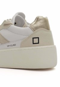Sneaker bianco con accenti testurizzati beige, tallone in oro metallico e dettaglio logo nero. Presenta una suola spessa in gomma bianca.