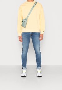 Sweat-shirt jaune avec poignets côtelés, jean bleu ajusté, et baskets blanches avec des accents verts. Petit sac bandoulière vert menthe.