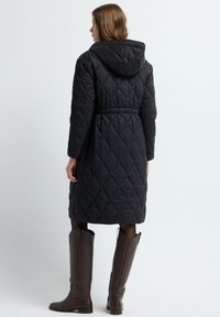 Quiltowany czarny długi płaszcz z kapturem, z paskiem w talii i wzorem w diamenty. Noszony z kontrastującymi brązowymi botkami do kolan.