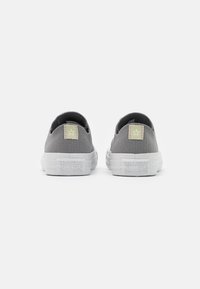 Para szarych trampek Converse All Star widoczna z tyłu na białym tle, ukazująca logo na pętli pięty i podeszwie.