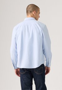 Lichtblauw overhemd met lange mouwen, een button-down kraag, een achterpand en een gebogen zoom, gecombineerd met donkere spijkerbroek.