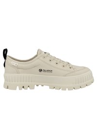 Beige canvas sneakers with thick rubber sole, textured grip pattern, and contrasting black heel tab. Features lace-up closure and logo detail.