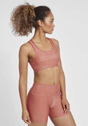 Lichtroze sportbeha met brede banden en het "HUMMEL" logo, gecombineerd met hoge, bijpassende shorts, beide gemaakt van een soepele stof.