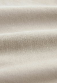 Tela de algodón beige con una textura suave, que presenta finos patrones de tejido diagonal y una calidad de caída suave.
