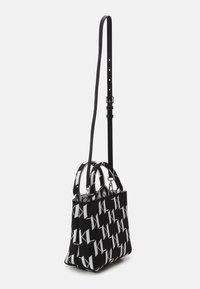Czarna i biała torebka z plecionego materiału, z powtarzającym się wzorem logo, podwójnymi uchwytami i regulowanym paskiem na ramię.