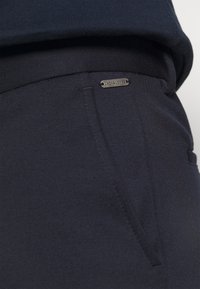 Marineblauwe joggingsbroek van zacht materiaal met een slim fit, voorzien van een zijzak en een metalen logoaccent op de tailleband.