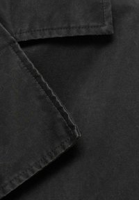 Material textil negru cu finisaj mat, evidențiind o secțiune pliată. Margini cusute cu atenție, subliniind o tăietură curată și durabilă.