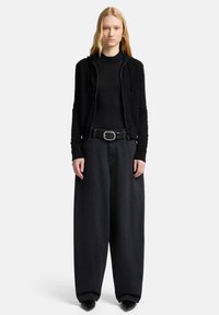 Czarna bluza z kapturem na zamek, noszona na dopasowanej czarnej koszulce, w połączeniu z luźnymi czarnymi spodniami dżinsowymi i czarnym paskiem z srebrną owalną klamrą.