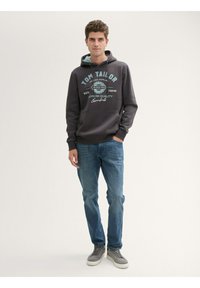 Sweatshirt gri cu text și logo turcoaz, cu buzunar tip kengur pe față, asociat cu blugi albaștri și adidași gri pe un fundal neutru.