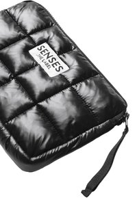 Schwarze gepolsterte Hülle mit glänzender Oberfläche, ausgestattet mit einem rechteckigen Etikett. Reißverschlussverschluss und abnehmbarer Tragegurt für einfaches Tragen.