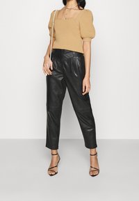 Top de punto beige con relieve, mangas abullonadas y escote cuadrado, combinado con pantalones de cuero negro de talle alto y tacones negros con tiras.