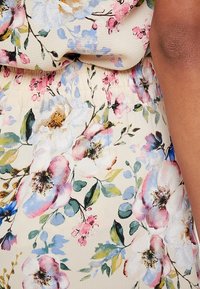 Tessuto floreale con grandi fioriture rosa e blu su sfondo beige, con foglie verdi e una cintura elastica texturizzata.