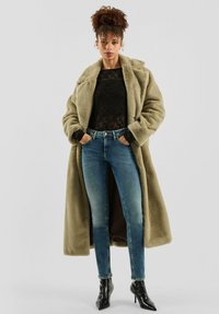 Długi płaszcz z oliwkowozielonego sztucznego futra, czarna koronkowa bluzka, niebieskie obcisłe jeansy i czarne szpiczaste botki za kostkę. Tkanina o fakturze i wyraźna konstrukcja.