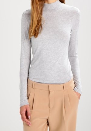 Vaaleanharmaa pitkähihaisen poolopaita pehmeästä, joustavasta neuloskankaasta, yhdistettynä beigeihin korkeavyötäröisiin housuihin, joissa on edessä laskokset.