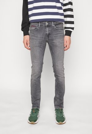 Mand iført falmede grå slim-fit jeans, grønne sneakers og en langærmet skjorte med sort-hvide horisontale striber.