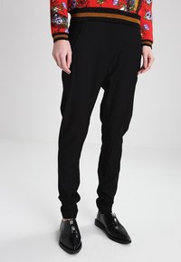 Svarta tapered byxor med sidofickor, tillsammans med svarta spetsiga skor med dragkedjor, och en röd blommig topp med midjeband i svart och guld.