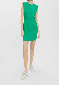 Zelené krátké šaty s krajkovými ramínky, elastickým pásem a hladkým povrchem. Spárované se světlými nazouvacími botami.