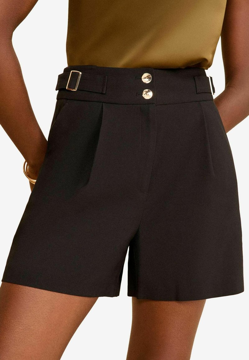 Shorts noirs ajustés avec une taille haute, présentant des plis avant, deux boutons en argent et un détail de ceinture pour l'ajustement.