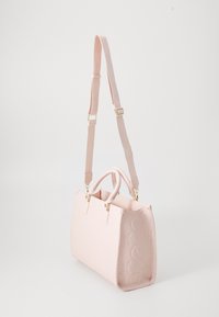 Sac à main rose clair avec des motifs floraux et circulaires en relief, deux poignées courtes et une bandoulière longue réglable sur un fond uni.