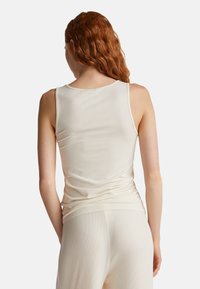 Ivory top na ramiączkach z lekkiego materiału, z dekoltem w kształcie łódki i dopasowanym krojem. Gładka tekstura z minimalną ilością szwów, w komplecie z dopasowanymi spodniami.