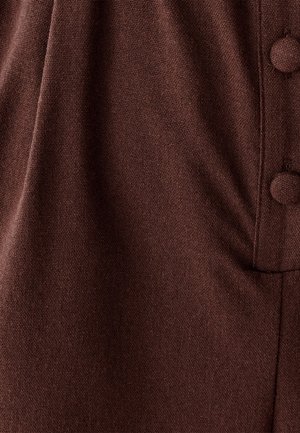 Bruine stof met een gestructureerde weving en een zachte uitstraling. Het kledingstuk heeft ronde knopen en een geplooid ontwerp.