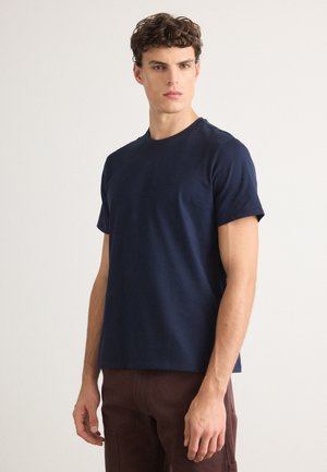 T-shirt bleu marine à col rond avec des manches courtes, fabriqué en tissu en coton. Présente une coupe décontractée et une texture lisse, design minimaliste.