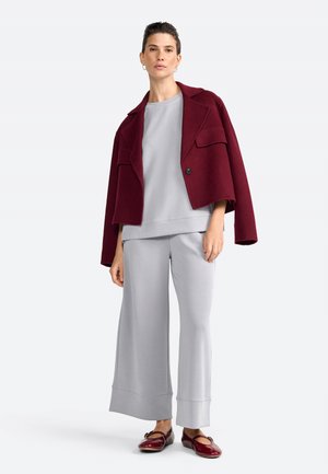 Burgundijas krāsas īsais žakets ar divām priekšējām kabatām virs gaismas pelēkā, brīva piegriezuma sporta krekla un atbilstošām platām biksēm. Sarkanas dzīvokļu kurpes.