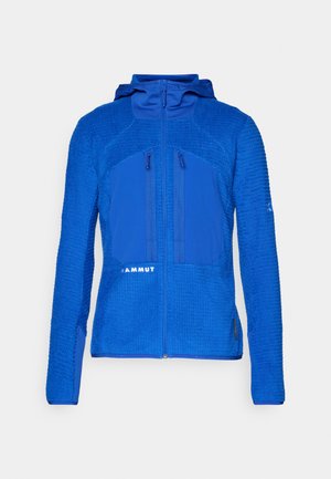 Chaqueta de forro polar azul con paneles superiores texturizados y paneles inferiores lisos. Cuenta con un cierre frontal y dos bolsillos con cremallera en el pecho.