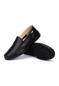 Zapatos negros de piel sin cordones con un acabado suave, paneles laterales elásticos y una suela de goma texturizada que presenta un patrón de relieve detallado.