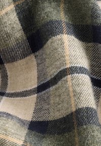Tissu en laine avec un motif à carreaux comprenant des nuances de beige, vert, bleu marine et de fines rayures jaunes dans un tissage doux et texturé.