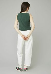 Haut sans manches vert associé à un pantalon large ivoire et des baskets Nike noires, roses et vertes. Design simple avec un style minimaliste.