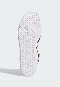 La suela de goma blanca de la zapatilla presenta un patrón de agarre texturizado con un acento de logo circular y tres rayas negras a lo largo del costado.