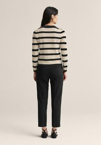 Musta ja beige raidallinen neule, jossa on pyöreä pääntie, yhdistetty mustiin housuihin ja mustiin nauhallisiin kenkiin, nähtynä takaa.