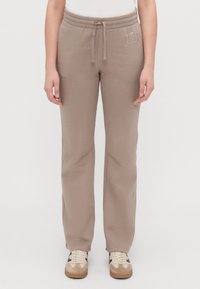 Pantaloni de jogging bej cu talie elastică și șnur. Prezintă logo-ul "GAP" brodat în bej mai deschis pe șoldul stâng. Textură moale.