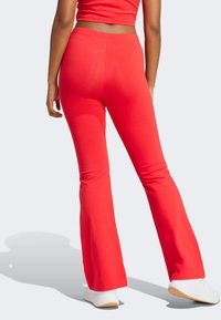 Röda utsvängda leggings tillverkade av stretchigt material, med hög midja och en slät yta, ihop med vita sportskor.