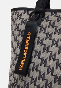 Gray fabric tote bag with a houndstooth pattern in black and beige. Features a black strap with "KARL LAGERFELD" in orange.