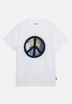 T-shirt en coton blanc avec un grand symbole de paix noir, incluant un graphique coloré de la Terre à l'intérieur du cercle. Étiquette visible sur le côté.