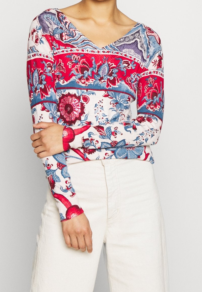 Haut à manches longues et col en V présentant un motif floral dynamique dans des teintes de rouge, bleu et blanc. Fabriqué en tissu doux avec des manches ajustées.