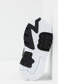 Semelle de basket noire et blanche avec caoutchouc texturé, motif de bande de roulement distinct et logo adidas sur le talon. Conception légère.