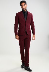 Burgundi színű, slim fit szabású öltöny, amelyhez illeszkedik a férfi zakó és egyenes szabású nadrág, fekete inggel és cipővel párosítva.