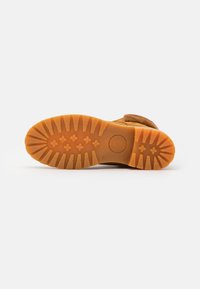 Bottine en daim marron avec une semelle en caoutchouc orange robuste, dotée de motifs de traction, conçue pour la durabilité et l'adhérence.