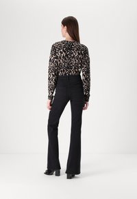 Black flared jeans with a high waist and back pockets, paired with a fitted long-sleeve top featuring a black and beige animal print.
