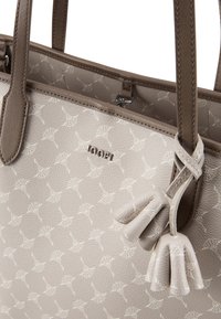 Borsa tote beige con una finitura testurizzata, caratterizzata da un motivo sottile. Include due dettagli in pelle a forma di nappa e un logo argentato.
