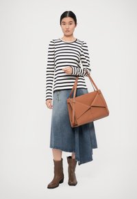 Brun lærveske med geometrisk design, brukt sammen med en svart og hvit stripete langermet skjorte og et jeansskjørt. Brune ankelstøvler.
