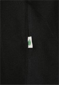 Svart stoff med en vertikal søm og en liten hvit merkelapp med et grønt løv-symbol delvis stukket inn i sømmen.